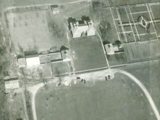 black and white aerial photgraph showing top of brick buildings and open fields with a geometric garden in upper right.