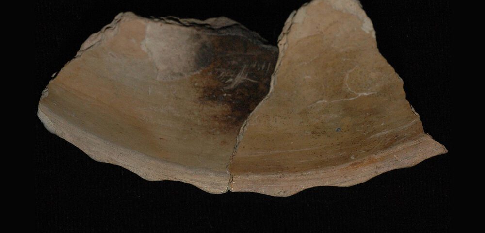 Partial rim of colonoware bowl with cut scalloped rim on black background