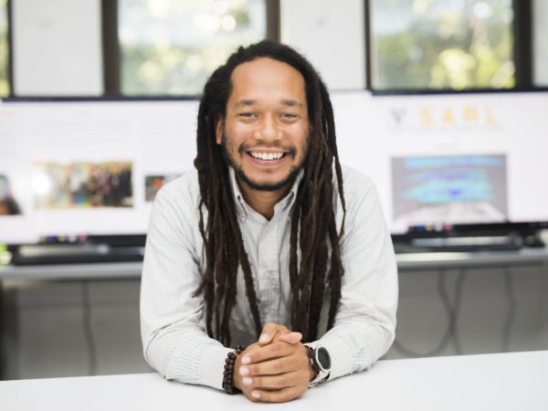 Man with dreadlocks sitting at a table with instructional area in background