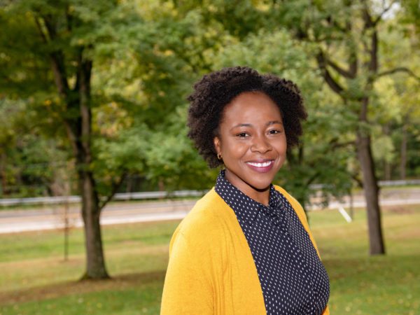 Woman with yellow cardigan, posed in a grassy area with trees