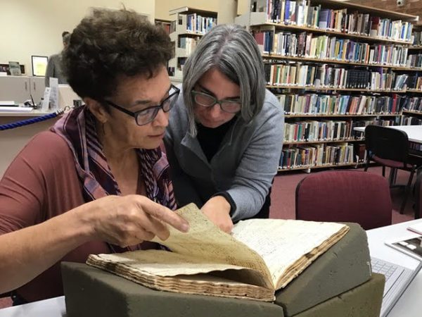 Two women, poring over a book in a library