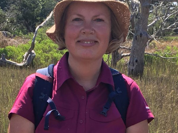 Woman with a pink shirt and straw hat, in fieldwork setting.