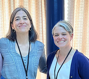 Two smiling women wearing lanyards, taken indoors
