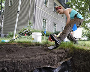 Woman excavating, with a house in the background