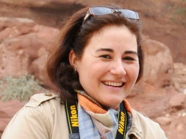 Woman posed outdoors in desert environment, with camera strap around neck