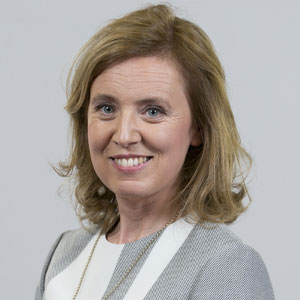 Close cropped headshot of a blonde woman with a neutral backdrop