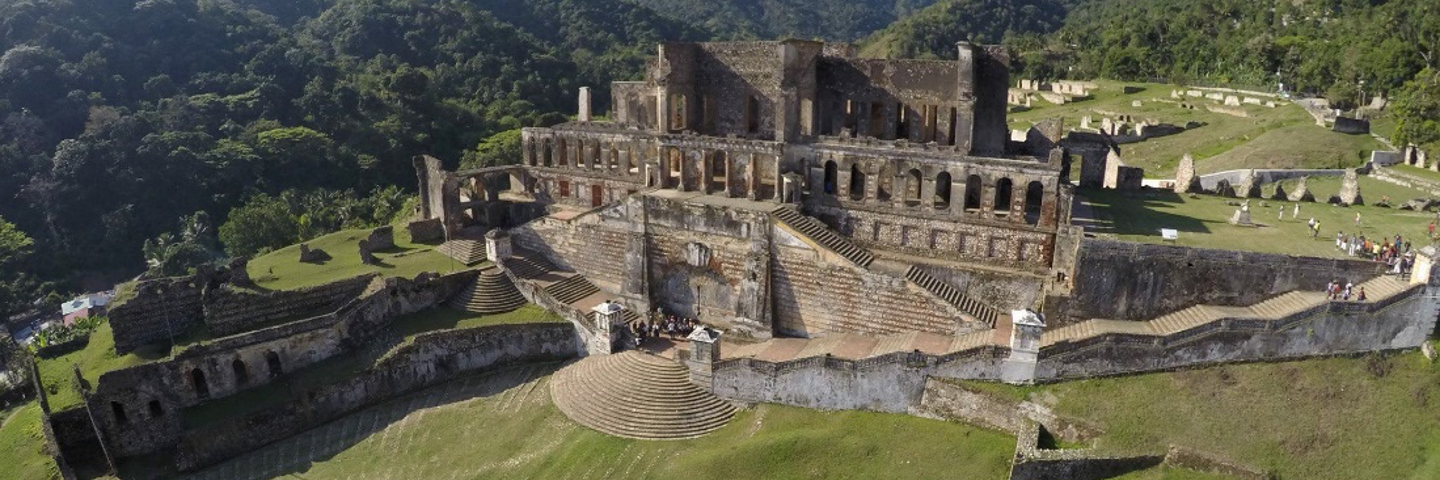 The ruins of a palace and terraced landscape with mountains and blue sky. Photo taken from above.