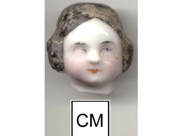 A porcelain female doll head with remnants of painted face and black hair.