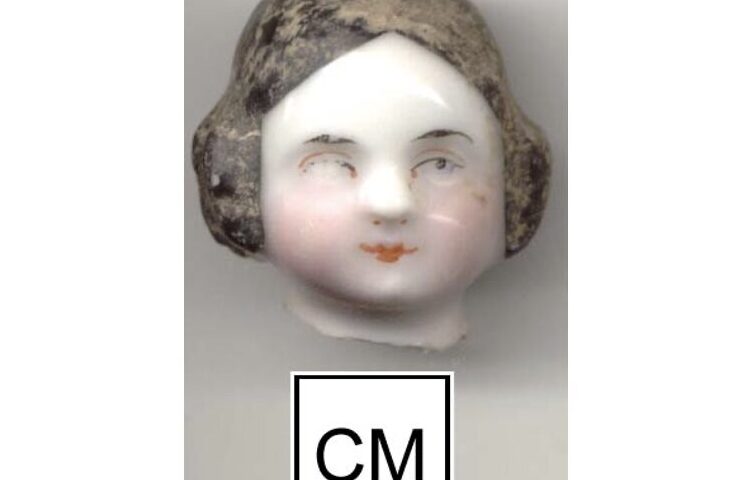A porcelain female doll head with remnants of painted face and black hair.